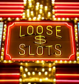Bright neon lights display the words 'Loose Slots' with a dollar sign in the center. The sign is outlined with bulbs, creating a vibrant and flashy effect typical of a casino or entertainment venue.
