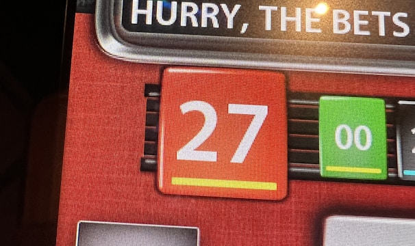 A digital display screen showing a casino betting interface, with text prompting to hurry bets and a highlighted number 27 in red. There are options for betting amounts and a 'share bets' button.
